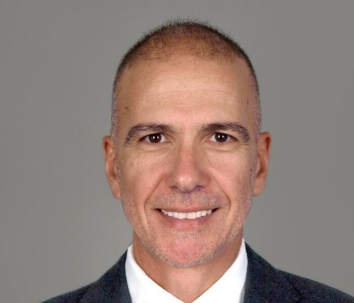Professional headshot of a man in a grey suit and striped tie against a neutral grey background.