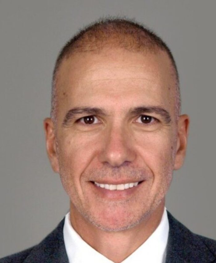 Professional headshot of a man in a grey suit and striped tie against a neutral grey background.